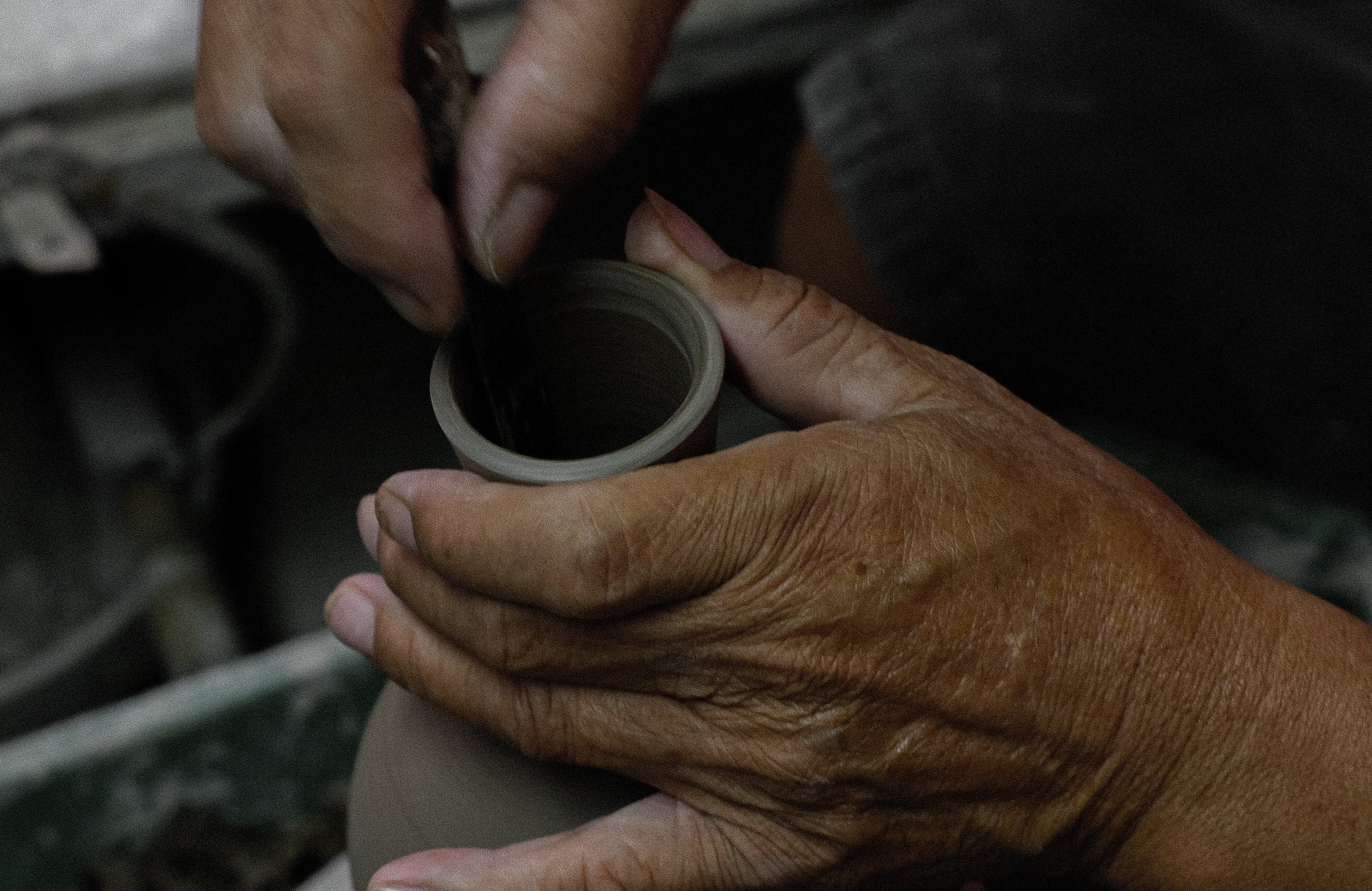 Close-up of a man trimming the mouth of a ceramic clay vase on a rotating throwing machine