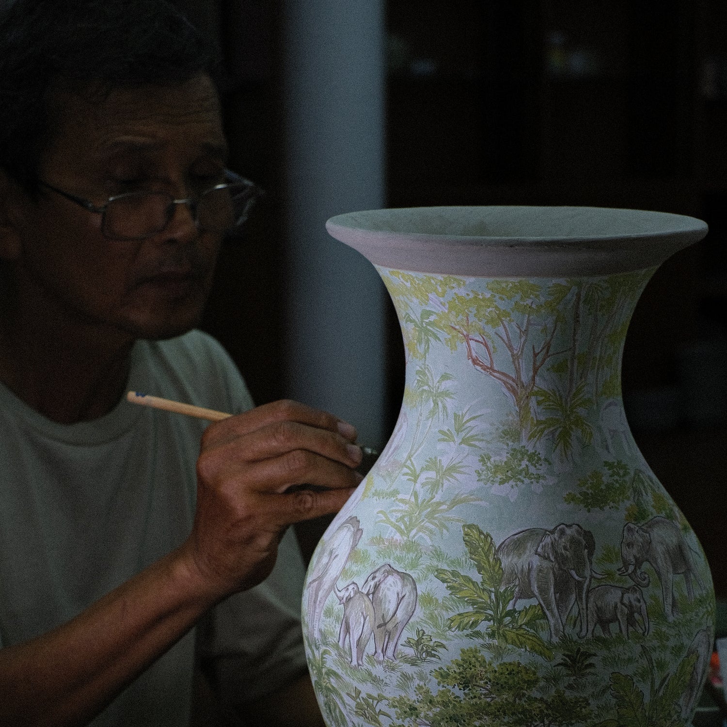 Man painting the details of the patterns for a family of elephants on a large vase